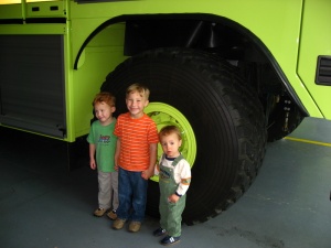 Three little boys by a large firetruck wheel